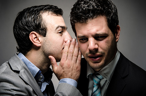 man whispering damaging rumors into someone's ear