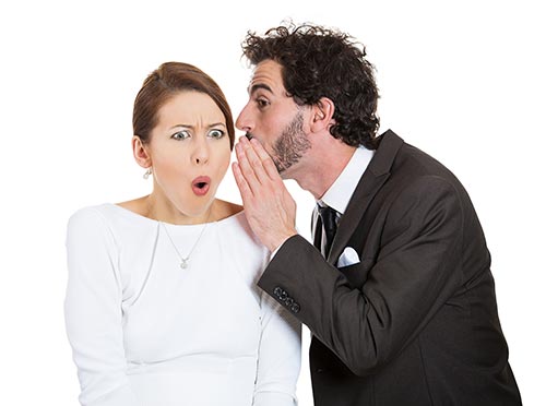 man whispering slanderous rumor into woman's ear